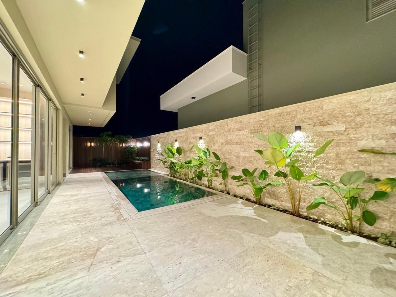 Terraço à noite com parede de travertino rockface iluminada e piso de travertino
